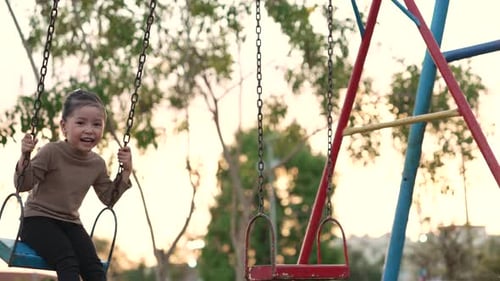 slow motion of cheerful child girl playing on a swing at playground