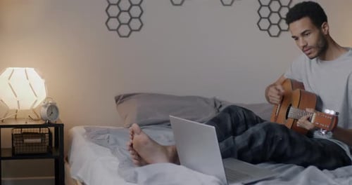 Young Man Plays Guitar on Bed at Home