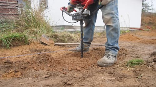 Ein Bauarbeiter bohrt auf einer Baustelle mit einem manuellen Bohrgerät ein Loch in den Boden