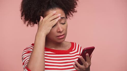 Stressed Woman Reading Bad News on Phone on Pink Background