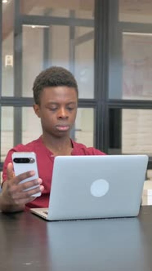Young Adult Working on Laptop with Phone