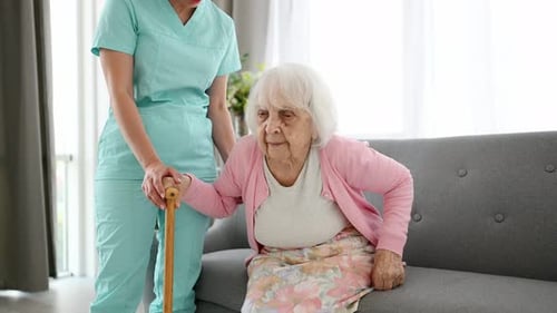 Caregiver Helping Senior Woman with Cane Stand Up