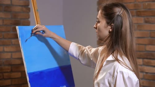 Woman Painting a Blue Landscape with Tool Indoors