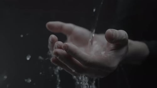 Hands Cupped Under Flowing Water in Dark Background