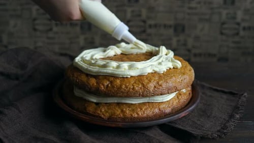 Chef decorating delicious homemade cake with whipped cream using pastry bag