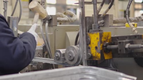Fabrikarbeiter mit Handschuhen bedient Maschinen mit Werkzeugen zum Biegen und Formen von Metallbauteilen