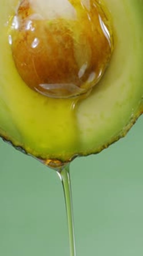 Oil is dripping down from cut in half avocado fruit.