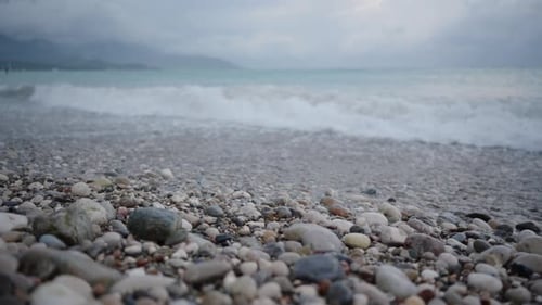 Overcast Weather in Blue Hues, Storm at Sea, Waves on a Pebble Beach, Close-Up. In Slow Motion.