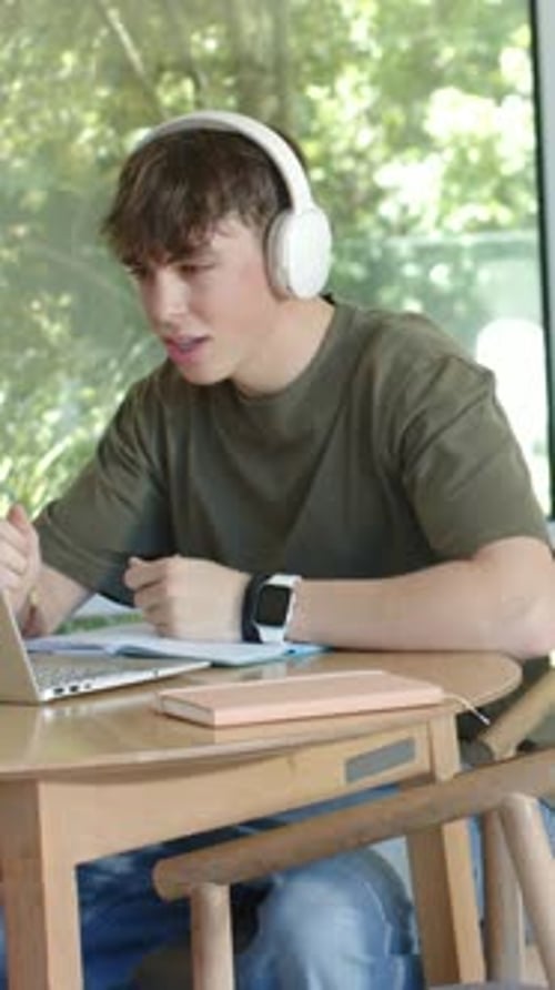 Vertical video: Joining call, teen in green tee wearing headphones speaking and noting at laptop
