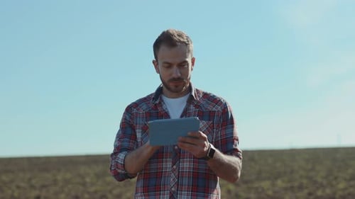 Portrait of Jouful Handsome Young Man Using a Tablet in the Large Endless Field Smiling Farmer