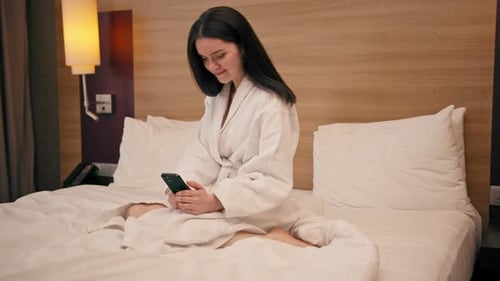 a young girl in a white coat in a luxury hotel room holds a smartphone and solves business issues