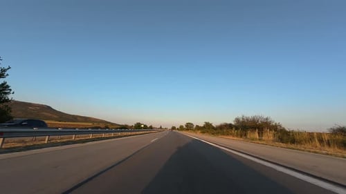 Driving on a Highway at Sunset with Clear Blue Sky Trees and Guardrails POV Car Perspective Summer
