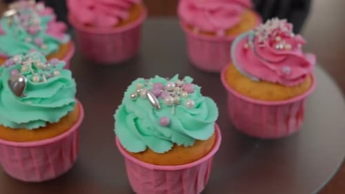 Closeup Tasty Muffins with Green and Pink Royal Icing Decorated with Edible Pearls Spinning on Tray