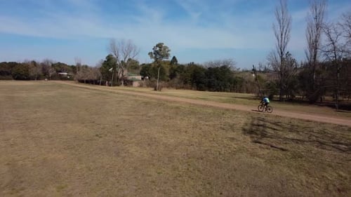 Professional cyclist pedaling his bicycle along cross country road in a field at sunset on a summer