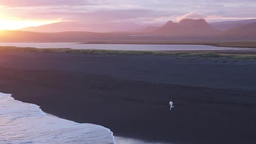 Man in White Suit Runs Fast Towards the Ocean on Reynisfjara Beach at Sunset