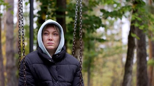 Portrait of a pensive woman with a beautiful face in the park on a swing