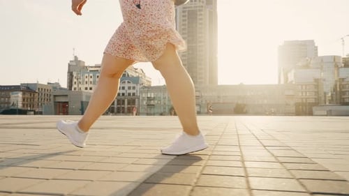 Women's Legs in White Sneakers Slowly Walk Along the City Street