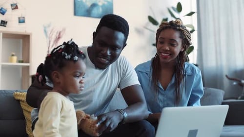 Young Parents Surf the Internet Via Laptop Their Little Daughter with Colorful Bows Joins Them