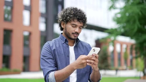 Handsome man uses a mobile phone while standing on the street near modern office building. Male