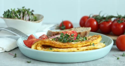 Woman eating tasty breakfast with omelette, microgreens and tomatoes at grey table, closeup