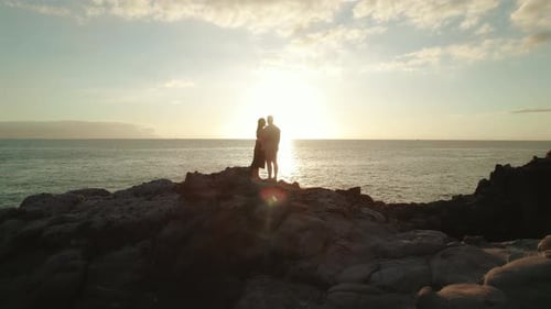 A couple stands together on the rocky coastline at Los Gigantes cliffs in Tenerife, Spain, embracing