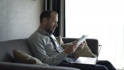 Handsome businessman works from home on sofa analyzing financial documents