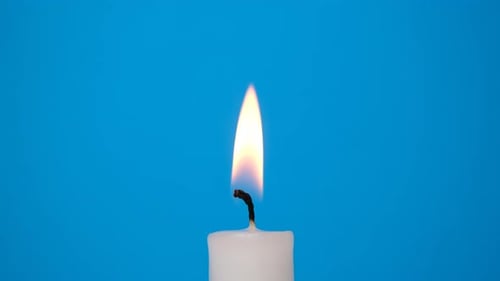 Close Up of White Candle Burning Against Blue Backdrop
