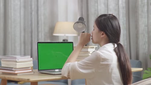 Bored Asian Teenager Yawning With Green Mock Up Screen Laptop While Doing Home Work