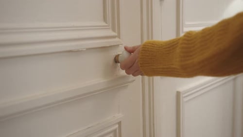 Close up shot of a female hands opening door by holding handle of the door inside a house.