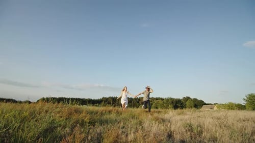 Romantic Stylish Couple Holding Hands and Running on Grassy Field in Countryside