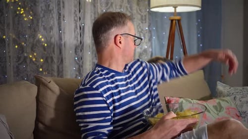 Man Eating Potato Chips on Couch at Night
