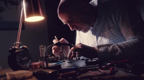 Man Working on Circuit Board at Desk at Night