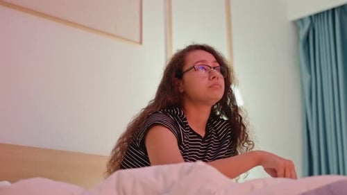 Woman in Hotel Bed Gazing Out Window at City Lights Bedside Lamp Glow Quiet Curtains Contemplative