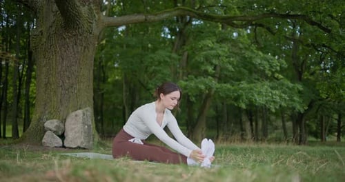 Young Beautiful Athletic Woman in Sportswear Doing Stretching and Warming Up in the Park Near a Tree