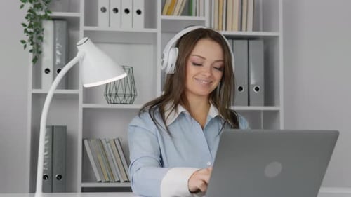 Woman Listens with Headphones at Laptop in Office