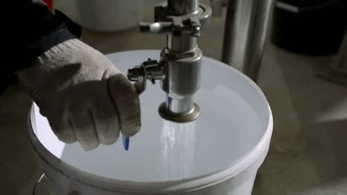 Manitas vertiendo agua en una lata de plástico en el taller de una planta, vista de cerca de la mano y el grifo