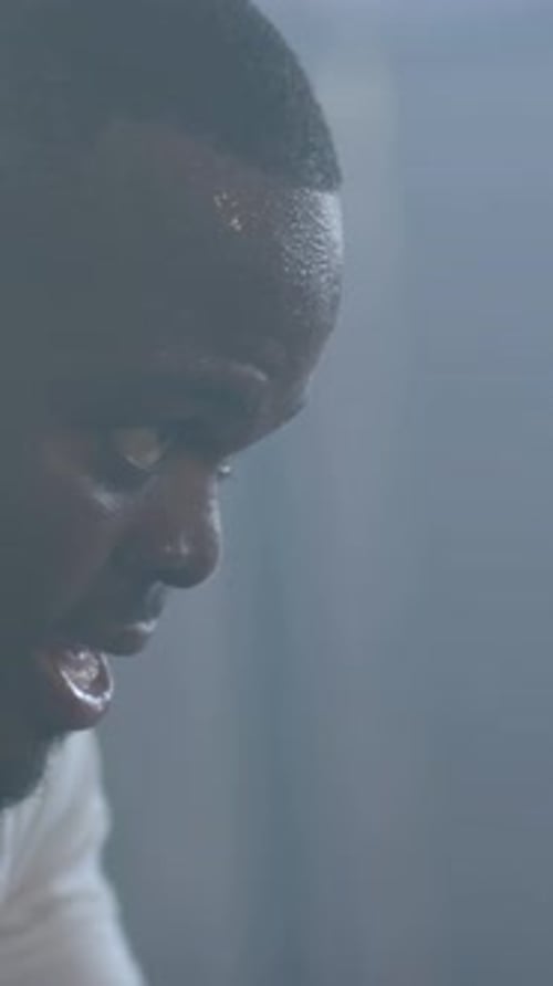 Vertical video: Panting adult man resting after set in gym, white tee, sweat beads, copy space