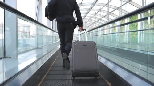 Unrecognizable Businessman with Suitcase on Rolls Runs on Escalator in Hall of Terminal Young Man is