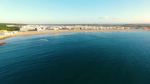 Aerial shot of the coastline with a town of white houses, sunny day and little waves in the sea. Bar