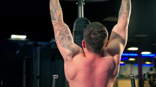 in the Gym Young Handsome Guy with Tattoos is Doing Pullups on the Horizontal Bar Shaking His Back