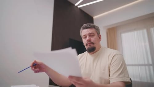 Man Sitting at Table Looking at Papers Thinking