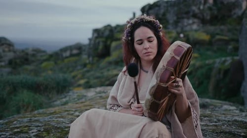 spiritual woman peacefully playing a shamanic drum in a beautiful medieval village medium shot