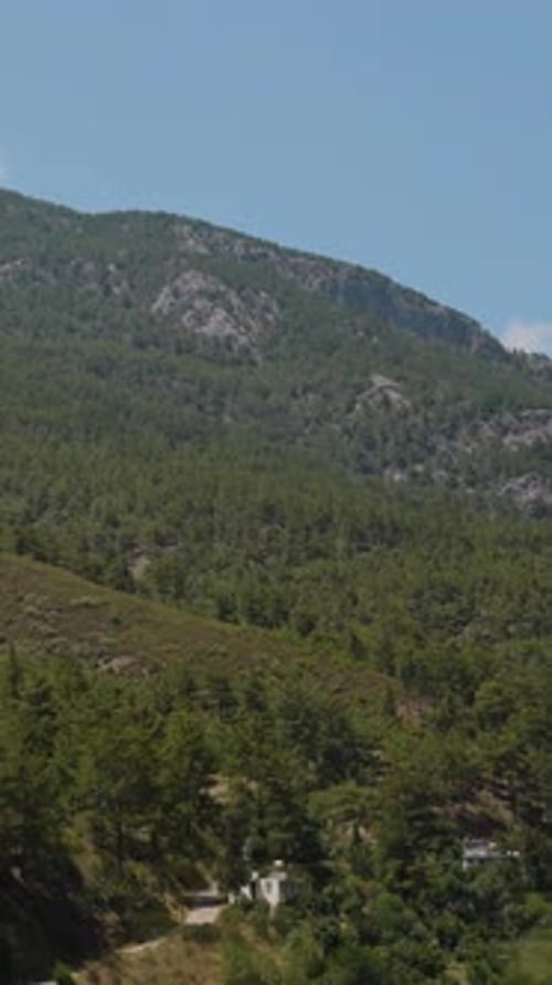 Vertical video. Driving Past Verdant Hills and Mountainous Terrain, a Serene Village Scene Unfolds