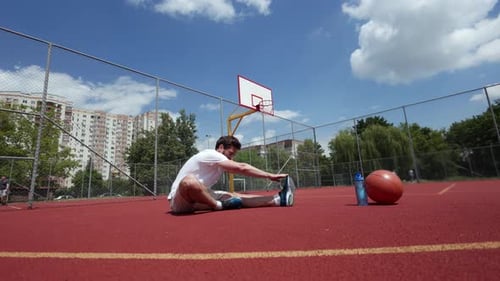 Fit Man Doing Stretching Exercises While Seated on Surface of Basketball Court