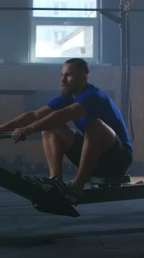 Focused Athlete Training on Indoor Rowing Machine in Dimly Lit Gym Emphasizing Strength Endurance