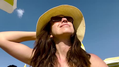 Frau mit Strandhut, mit dem Gesicht zur Sonne sitzend, Sommer, Urlaub, Poolzeit 4k, Ansicht von unten