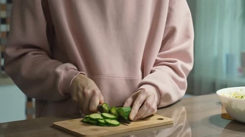 Woman Slicing Cucumber on Cutting Board in Kitchen