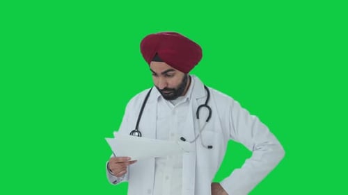 Stressed Sikh Indian doctor checking medical reports Green screen