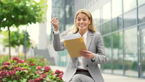 Excited businesswoman reading letter with great news sitting on a bench on the street near an office