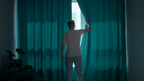 Man Opens Curtains to City View, Stretches